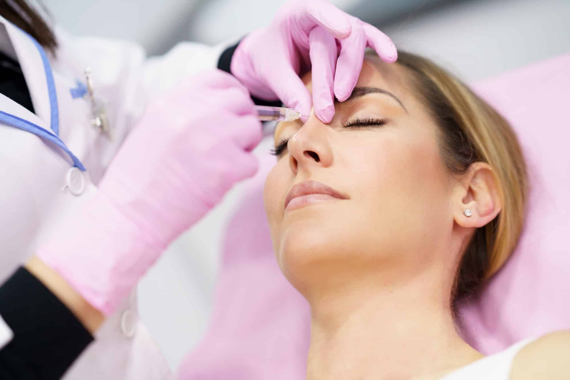 Doctor performing rhinoplasty by injection of hyaluronic acid in the nose of his patient